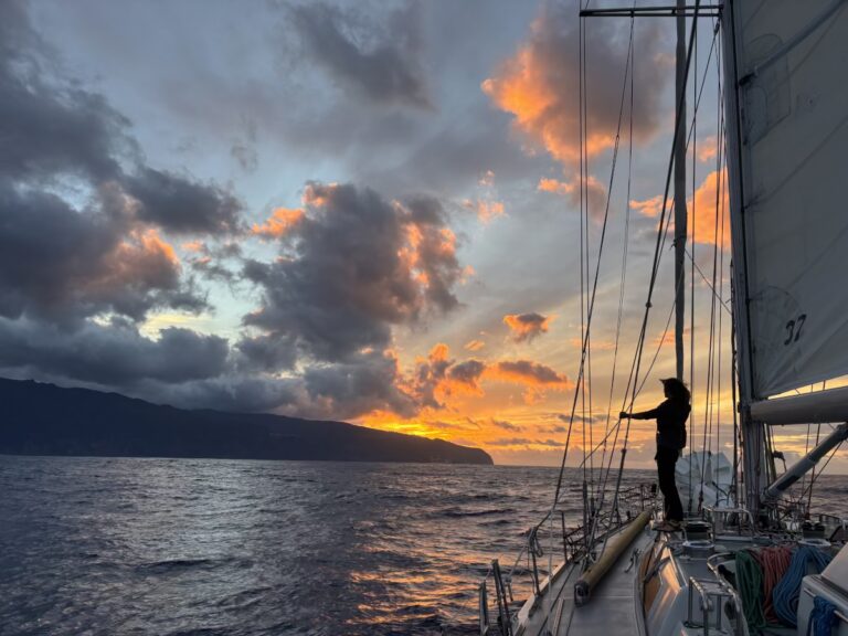 Sailboat at golden hour with distant lighthouse